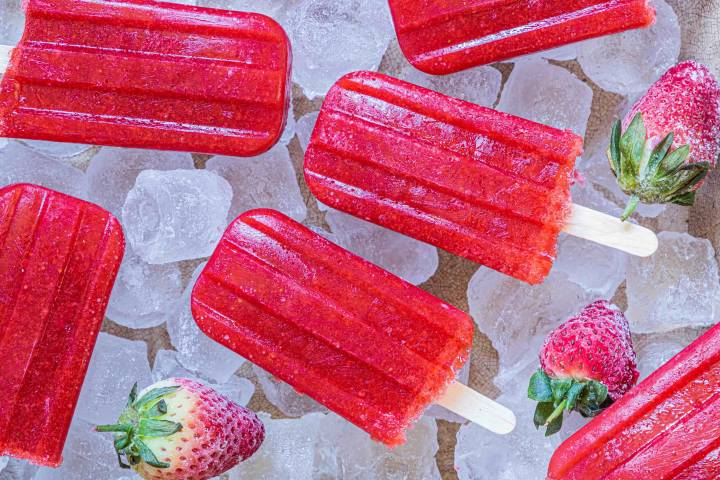 Bright red strawberry popsicles on ice, accompanied by fresh strawberries, create a refreshing summer treat scene.