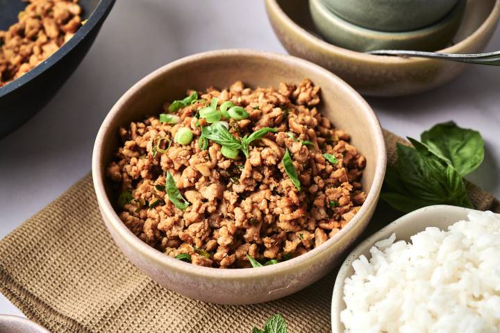 A bowl of seasoned ground meat topped with green onions and basil, served alongside a side of fluffy white rice.