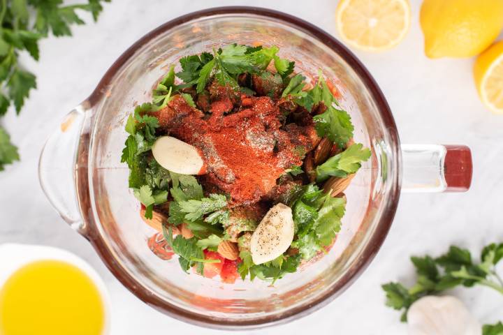 Ingredients for romesco sauce in a blender including garlic, parsley, almonds, and paprika.