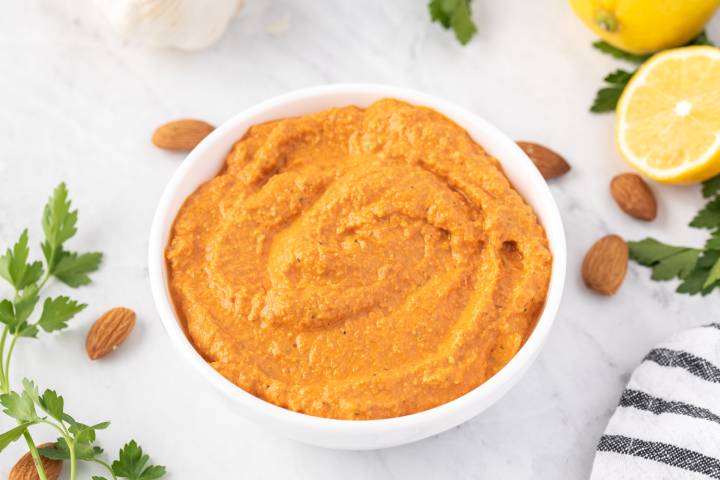 Spanish romesco sauce in a bowl with almonds, lemons, and parsley on the side.