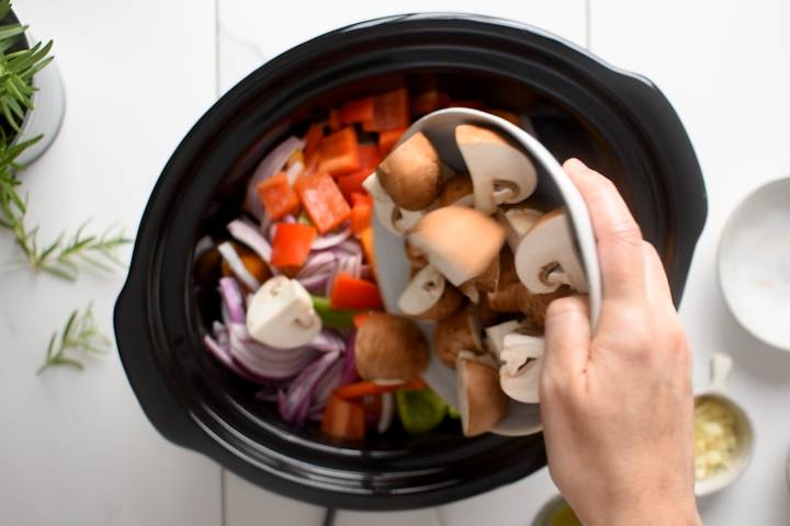 Vegetables and herbs being added to a slow cooker for ratatouille.