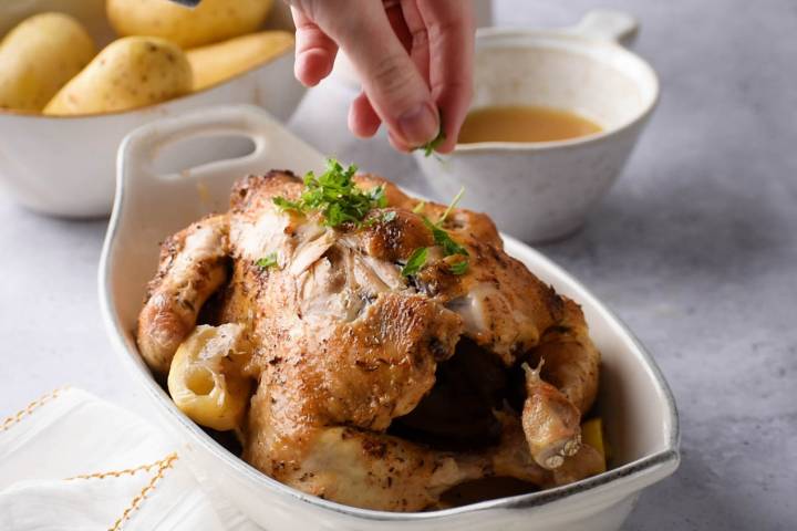 Crockpot rotisserie chicken with lemon and spices being sprinkled with parsley.