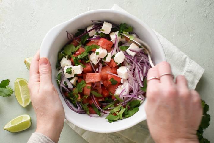 Cubes of watermelon, feta cheese, red onion, and cilantro being stirred in a bowl.
