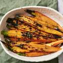 A white bowl filled with charred orange carrots topped with herbs, resting on a green cloth and surrounded by a textured surface.