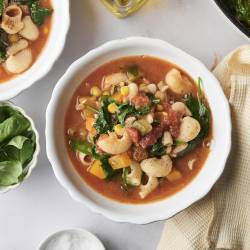 A cozy bowl of garden minestrone packed with shell pasta, corn, spinach, white beans, and vibrant vegetables in a savory tomato broth.