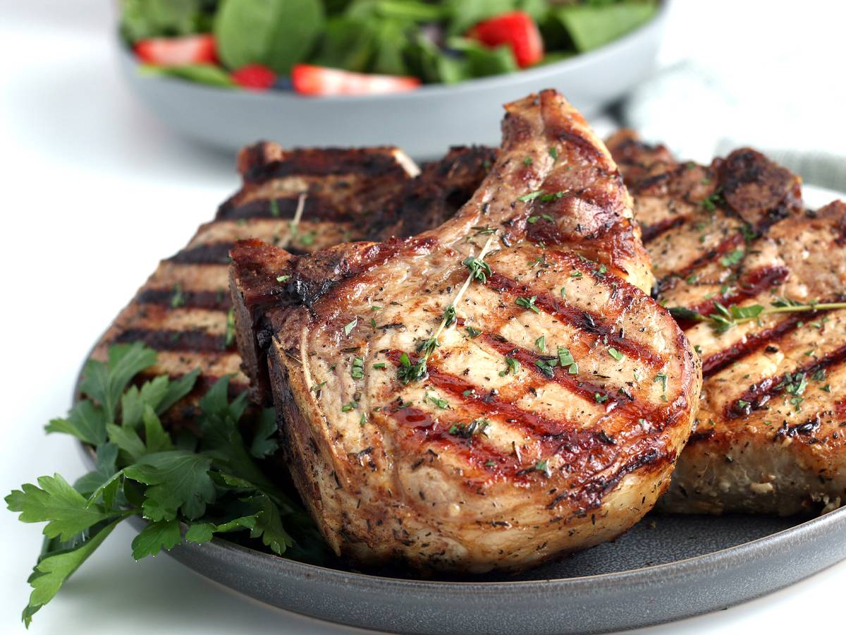 Grilled pork chops with grill marks and fresh thyme on a plate.