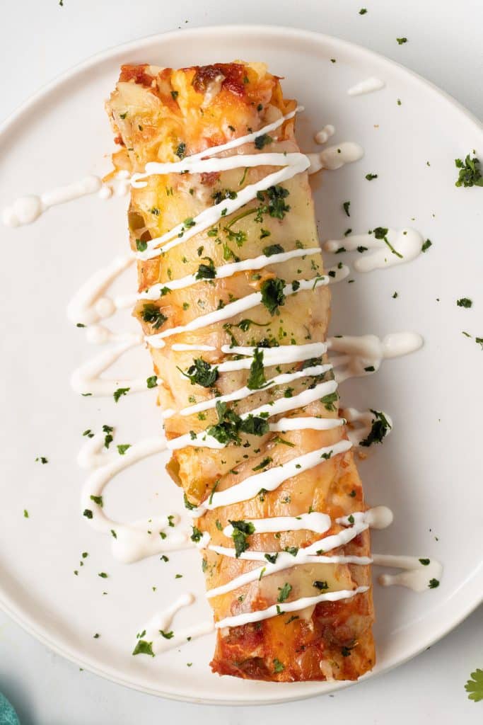 overhead shot of an enchilada on a white plate drizzled with sour cream.