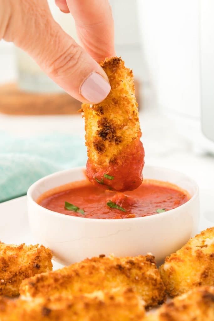 hand dipping a mozzarella stick into marinara.