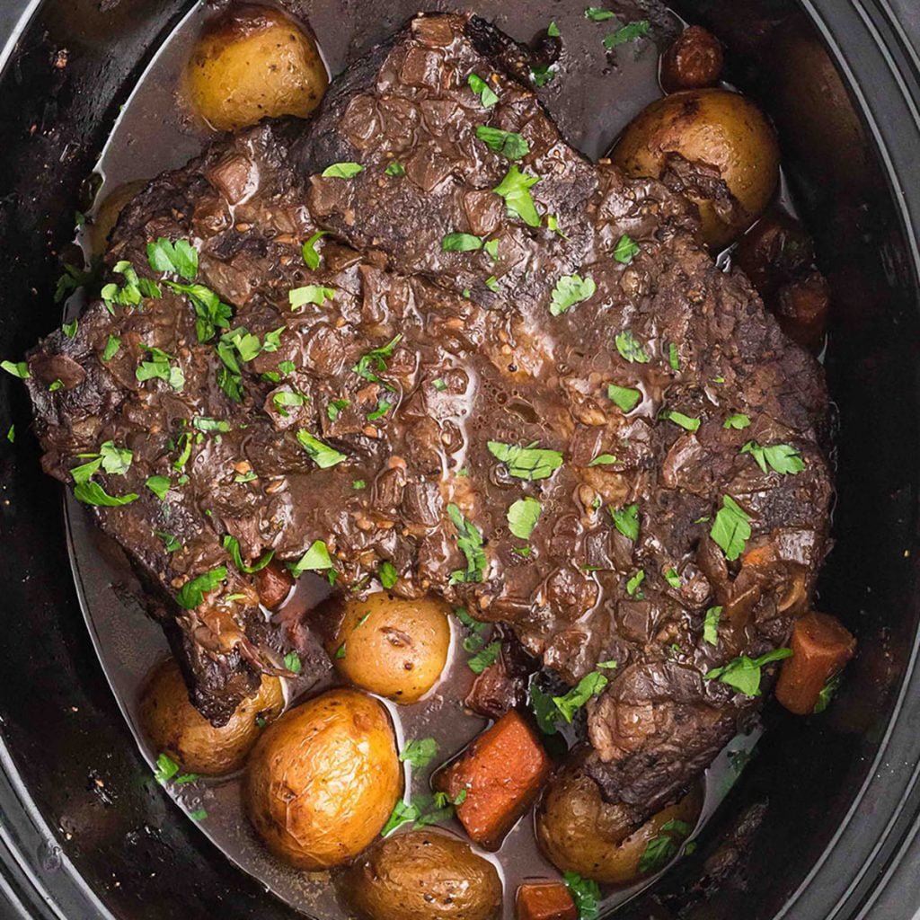 overhead shot of roast beef, potatoes, and carrots in a crock pot.