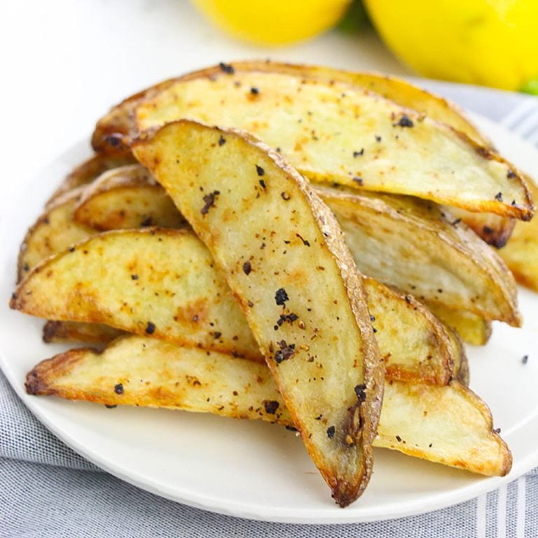 closeup of seasoned baked potato wedges on a white plate.