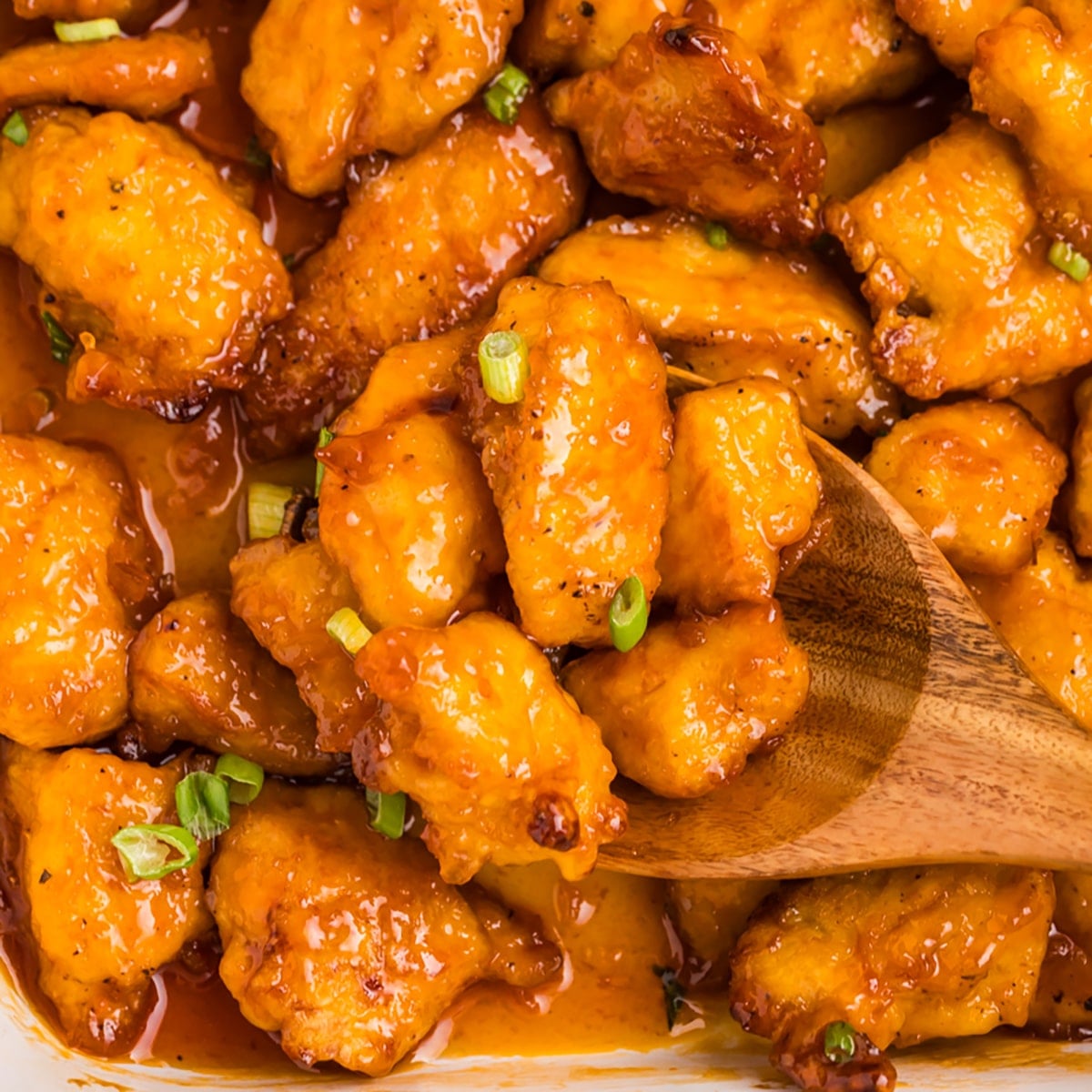 wooden spoon lifting a scoop of sweet & sour chicken.