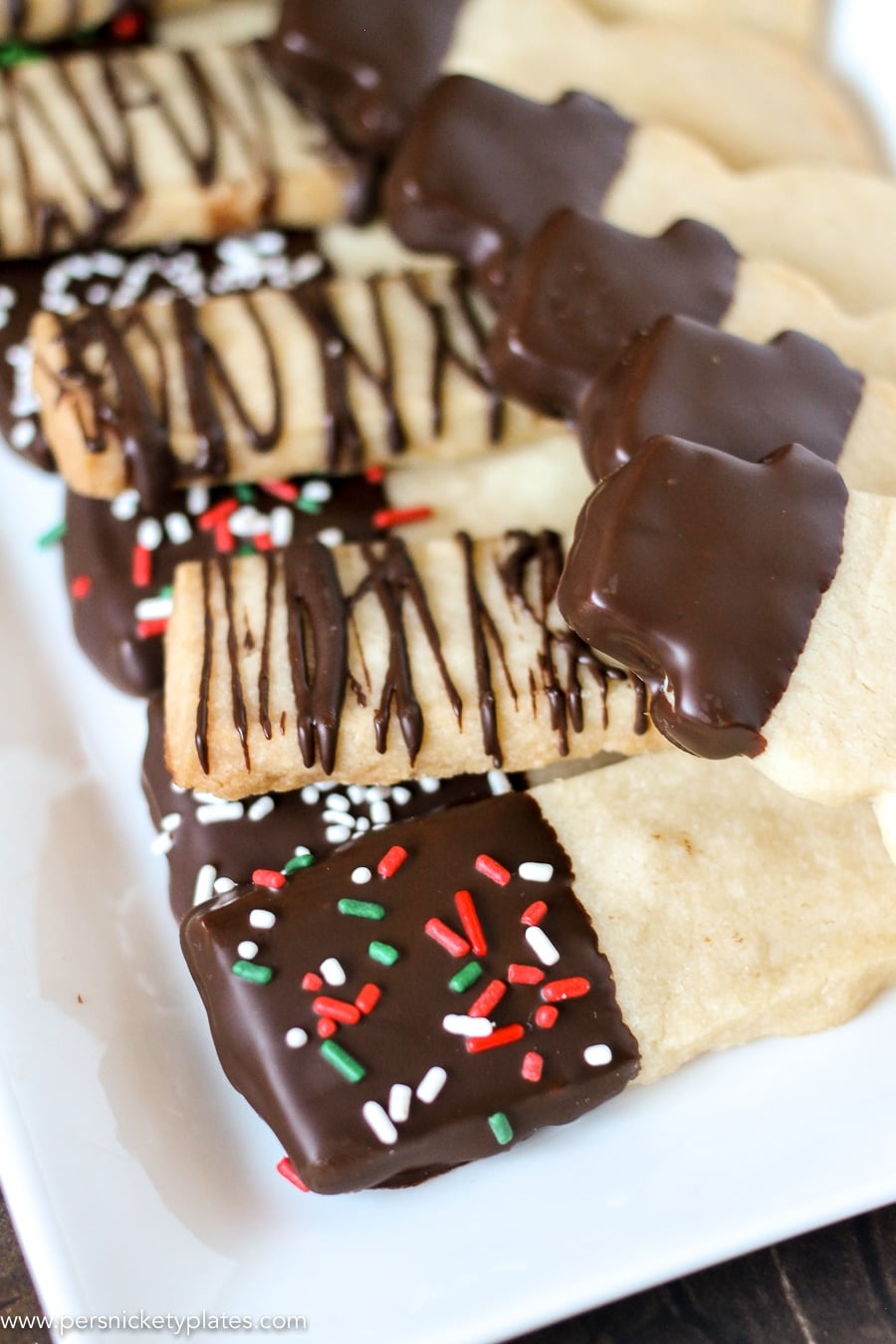 Chocolate Dipped Shortbread Cookies are a simple, from-scratch, shortbread cookie dipped in dark chocolate that's perfect for dunking in milk, coffee, hot chocolate...Santa won't be disappointed with these shortbread Christmas cookies! | www.persnicketyplates.com #christmascookies #shortbread #easyrecipe #baking #cookies #chocolate #sprinkles platter of chocolate dipped shortbread cookies with christmas sprinkles