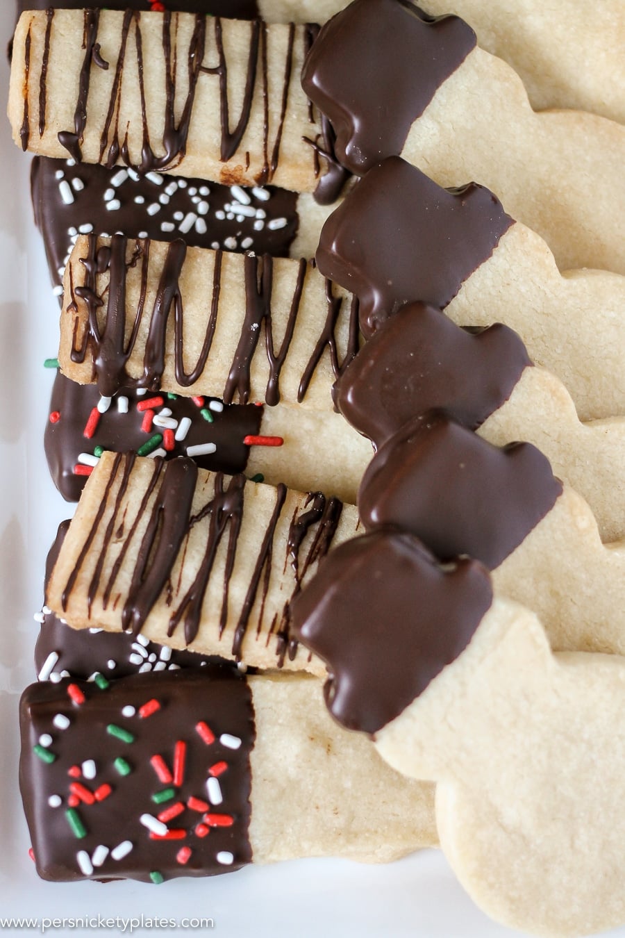 Chocolate Dipped Shortbread Cookies are a simple, from-scratch, shortbread cookie dipped in dark chocolate that's perfect for dunking in milk, coffee, hot chocolate...Santa won't be disappointed with these shortbread Christmas cookies! | www.persnicketyplates.com #christmascookies #shortbread #easyrecipe #baking #cookies #chocolate #sprinkles platter of chocolate dipped shortbread cookies in rectangles & snowman shapes