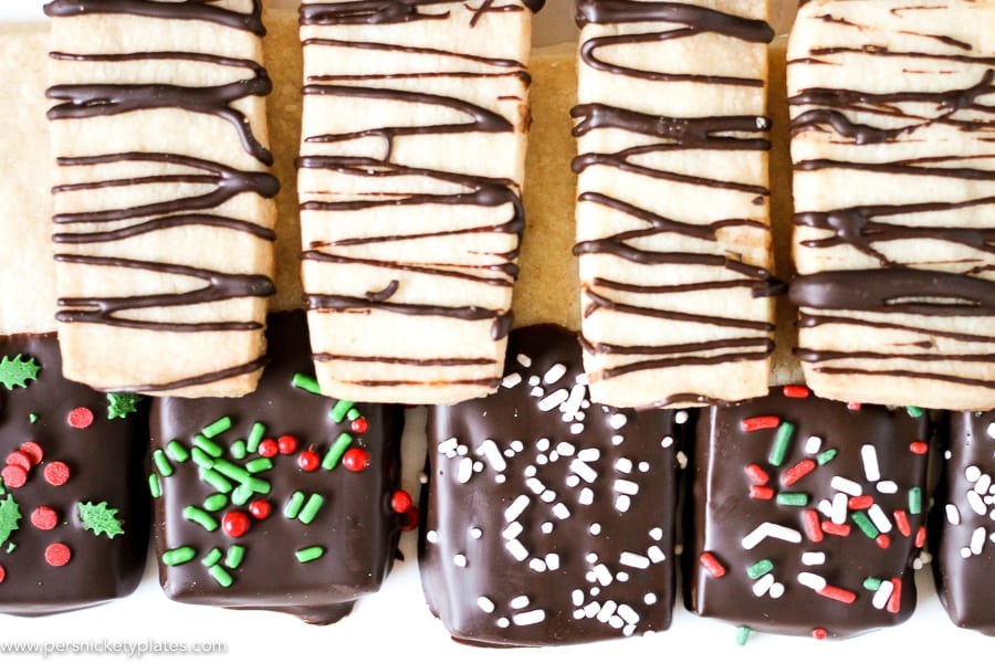 Chocolate Dipped Shortbread Cookies are a simple, from-scratch, shortbread cookie dipped in dark chocolate that's perfect for dunking in milk, coffee, hot chocolate...Santa won't be disappointed with these shortbread Christmas cookies! | www.persnicketyplates.com #christmascookies #shortbread #easyrecipe #baking #cookies #chocolate #sprinkles platter of shortbread cookies with chocolate and christmas sprinkles