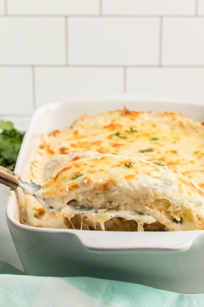 spatula lifting an enchilada from a baking dish.