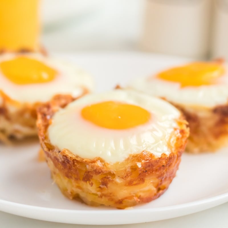 Bird's Nest Breakfast Cups are a fun way to eat eggs and hash browns for breakfast. These baked egg cups combine hash browns and cheese to form a "nest" and are topped with an egg. | www.persnicketyplates.com three hash brown egg cups on a white plate