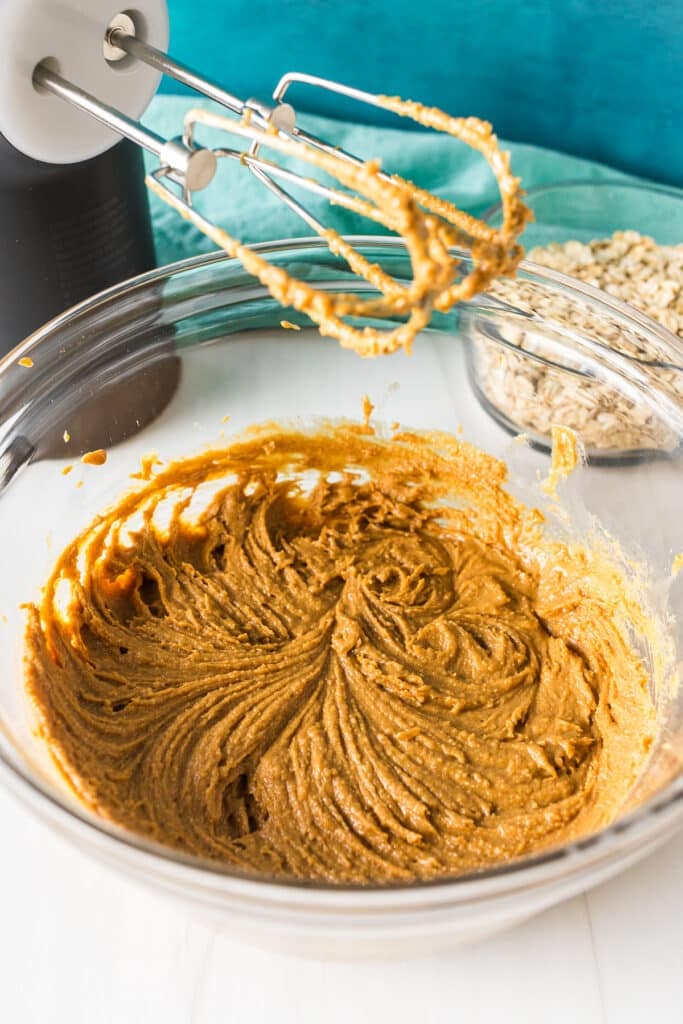 mixing bowl with peanut butter next to a hand mixer.