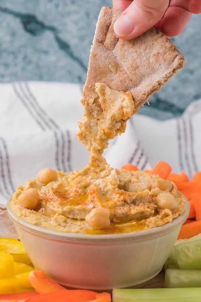 hand dipping pita bread into a bowl of hummus.