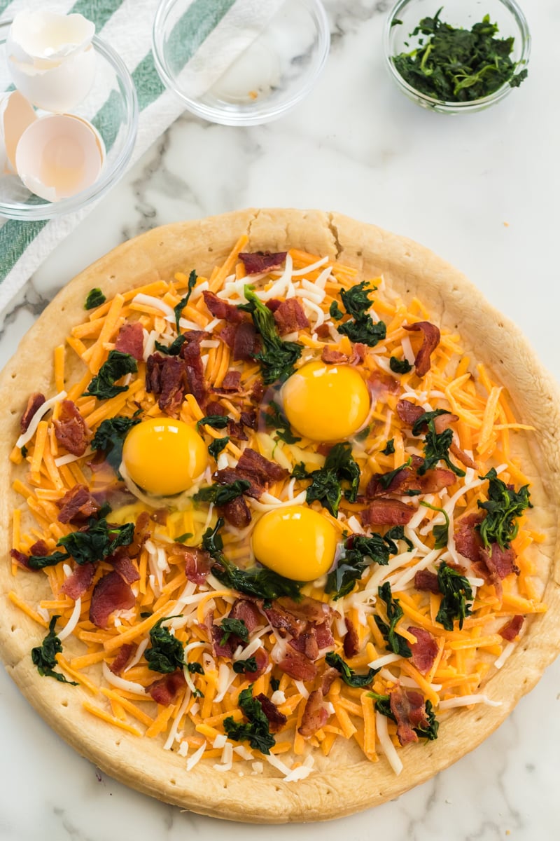 Bacon & spinach breakfast pizza is a filling and unique way to start your day. Pizza for breakfast is always a good idea! | www.persnicketyplates.com #pizza #breakfast #breakfastpizza #easyrecipe eggs cracked on breakfast pizza