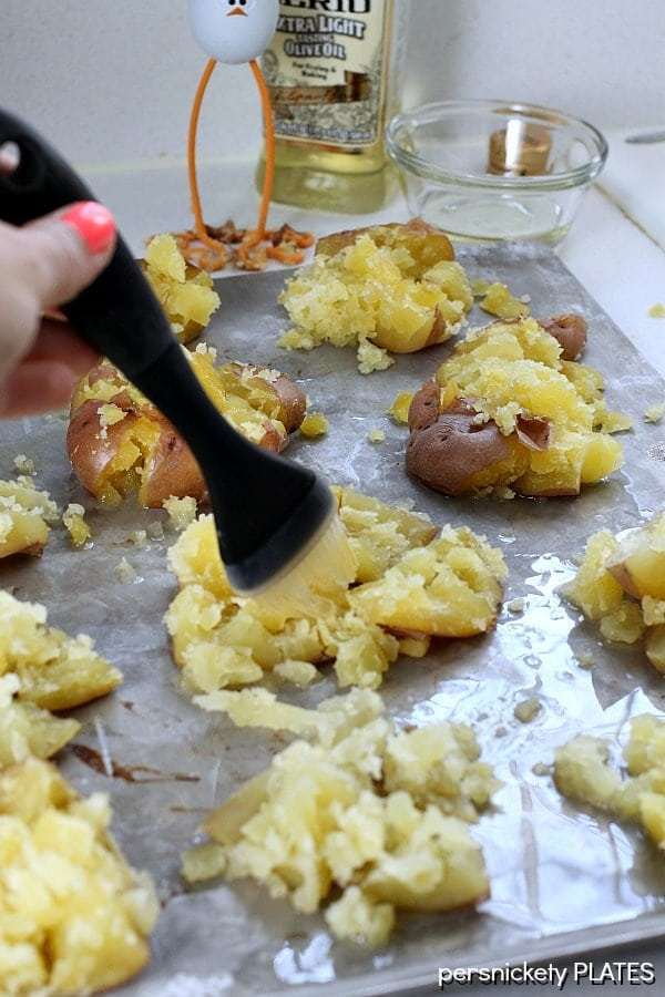 Crash Hot Potatoes are like a mix of a fluffy baked potato and a crispy french fry. The perfect side dish for your next dinner! | www.persnicketyplates.com #potatoes #sidedish #vegetarian #easyrecipe brushing olive oil and crash hot potatoes