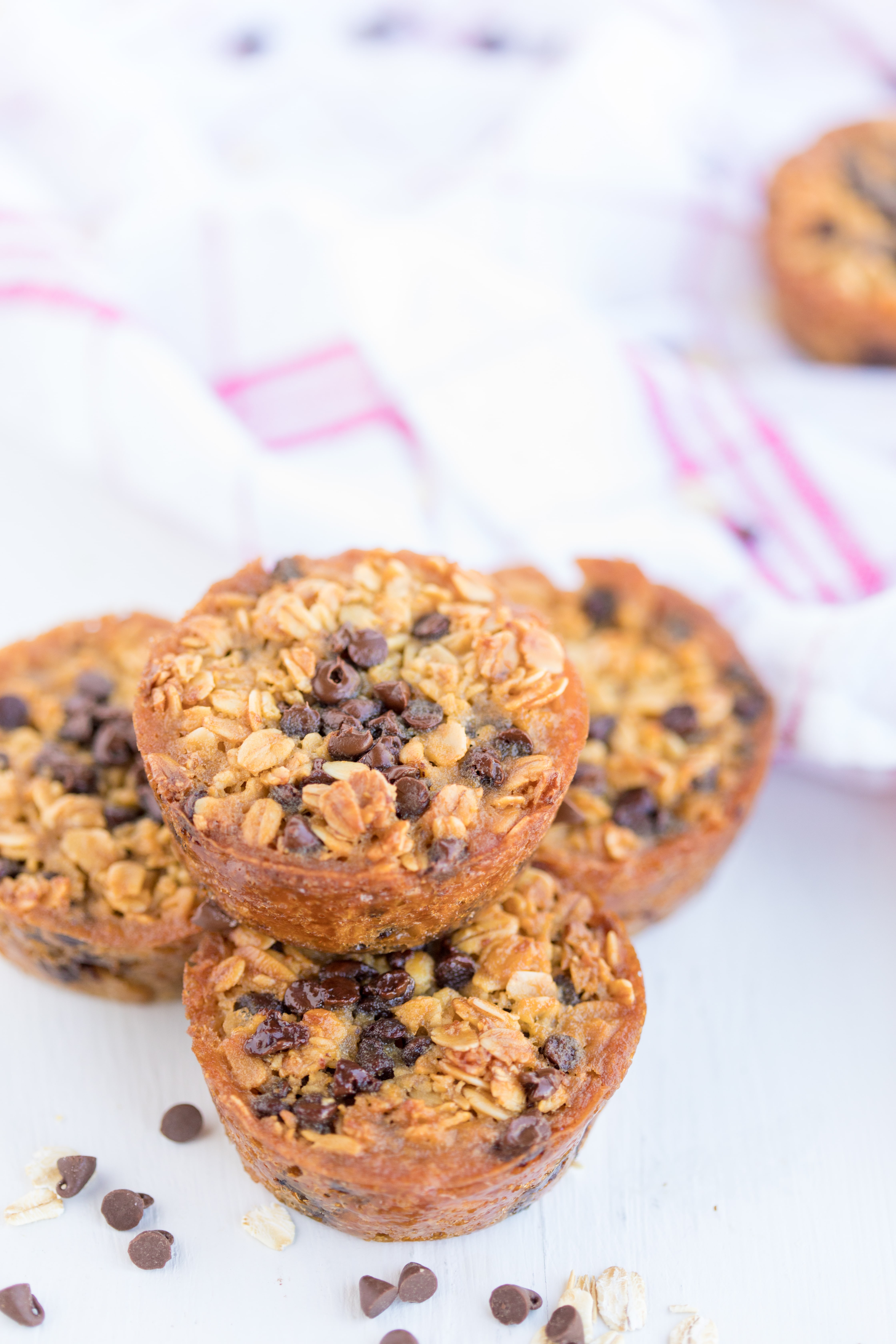 Baked Oatmeal Chocolate Chip Breakfast Cups are the perfect option for on-the-go breakfast! Swap out the chocolate chips for fruit, nuts, or spices for variety. | www.persnicketyplates.com stack of 4 Baked Oatmeal Breakfast Cups surrounded by mini chocolate chips