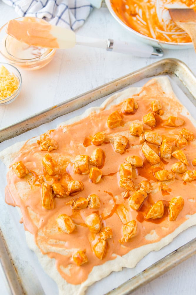 pizza crust topped with buffalo sauce and cooked chicken