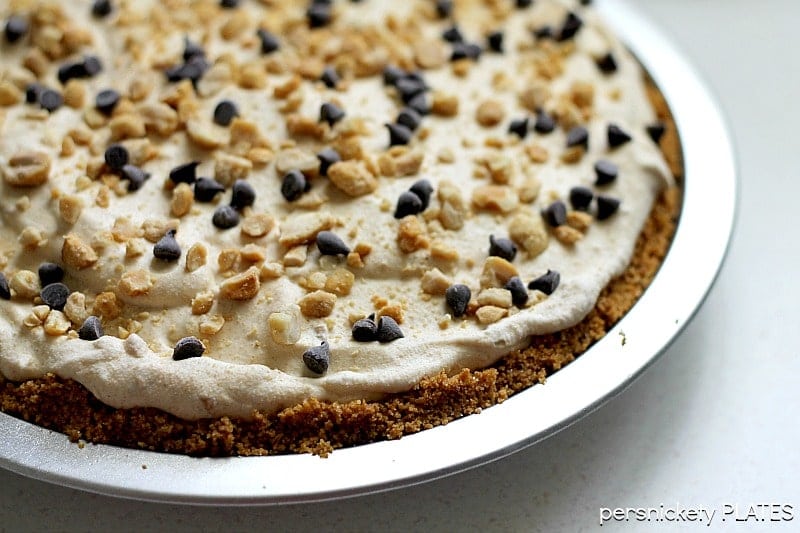 whole frozen peanut butter pie in pie plate peanut butter pie in a metal pie plate topped with crushed peanuts and mini chocolate chips.