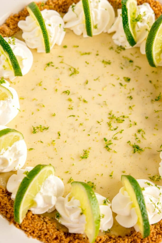 closeup shot of a key lime pie topped with lime zest, lime slices, and whipped cream.