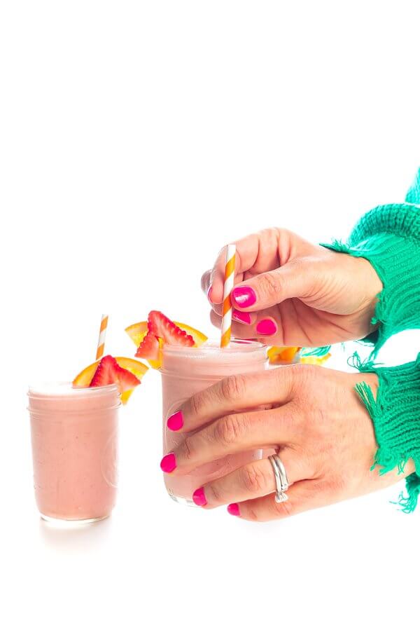 Holding a mason jar of strawberry sunrise breakfast smoothie.