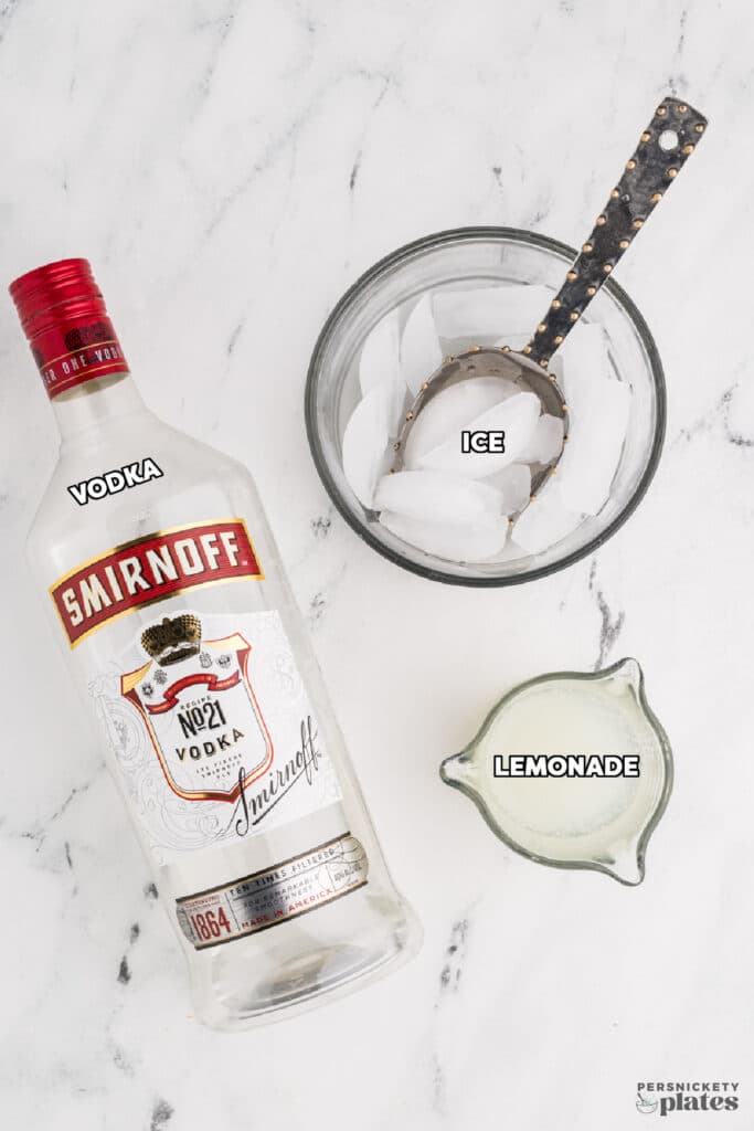 A bottle of vodka, a bowl of ice, and a small pitcher of lemon juice on a marble surface.