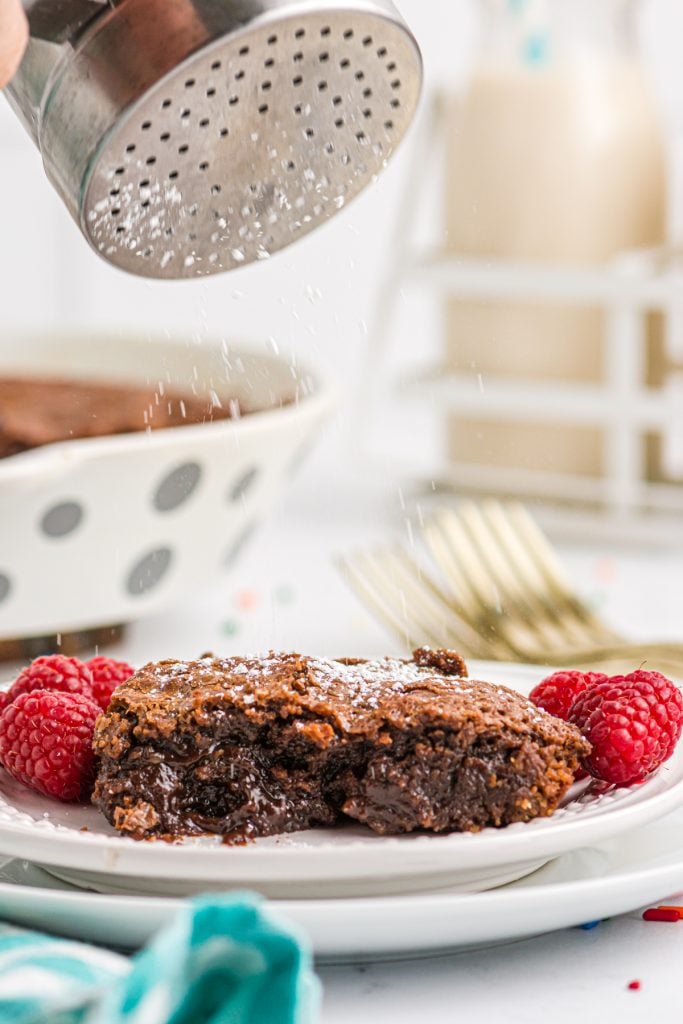powdered sugar being shaken onto a slice of fudge pie.