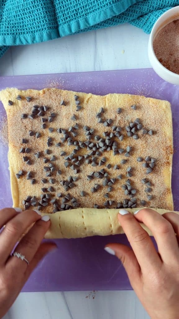 hand rolling up cinnamon roll dough with mini chocolate chips.