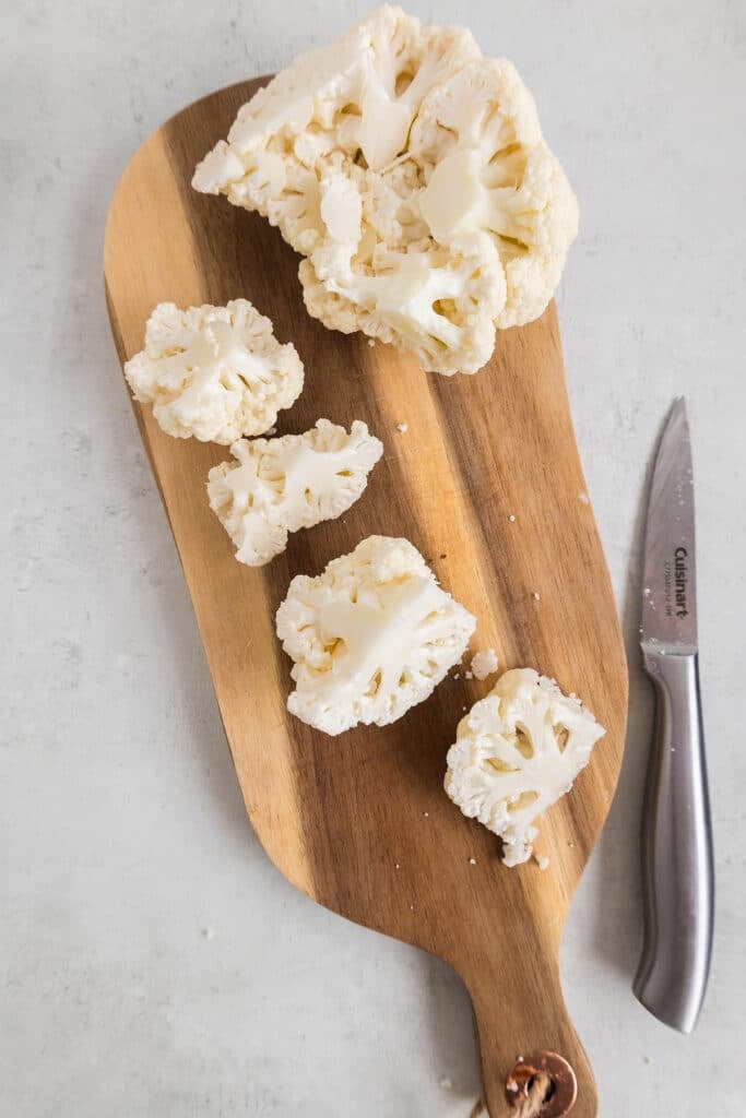 head of cauliflower cut into florets on a board.