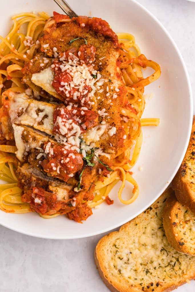 sliced mozzarella chicken breast on a bed of fettuccine.