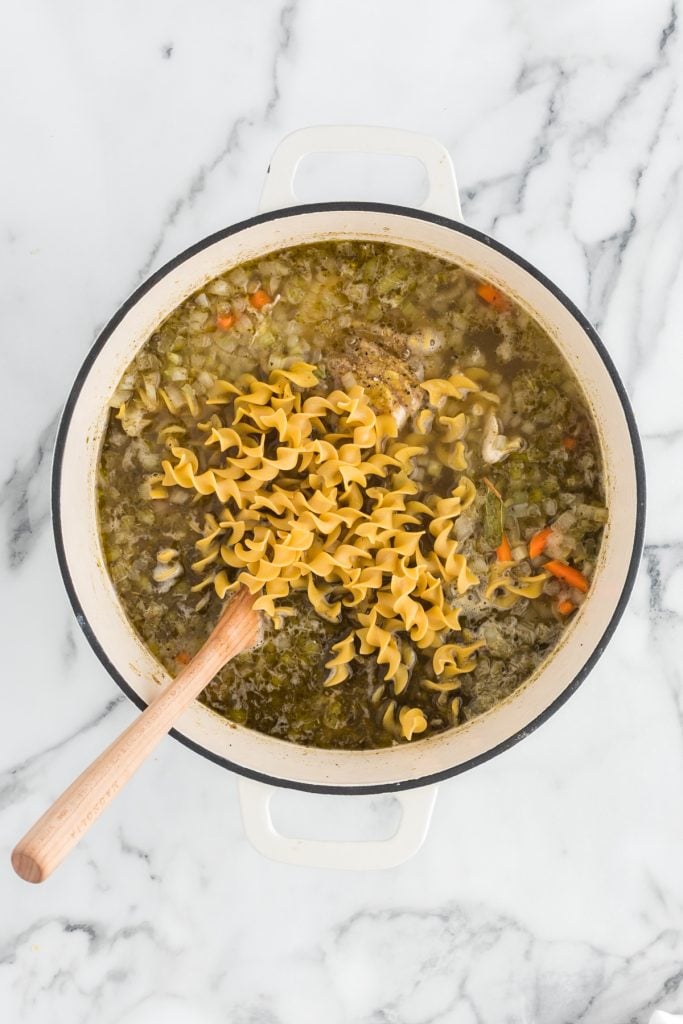 overhead shot of pot of chicken noodle soup with wooden spoon