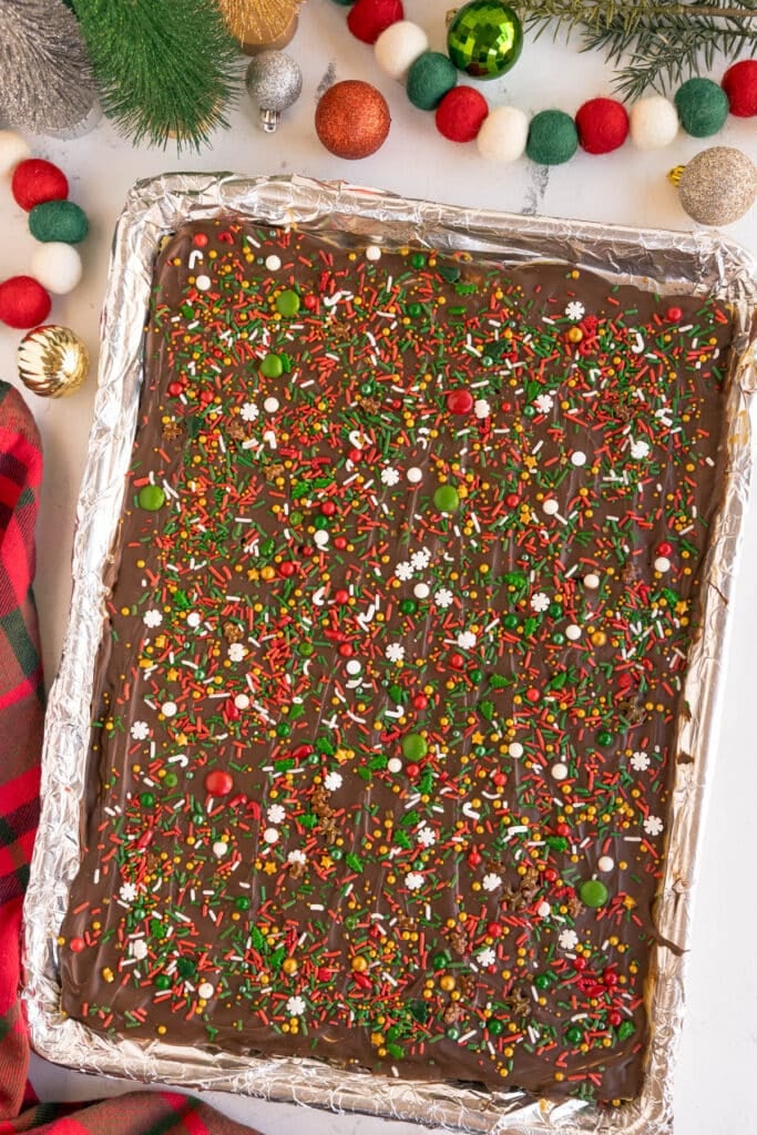 A baking tray of chocolate-covered Christmas crack decorated with colorful holiday sprinkles.