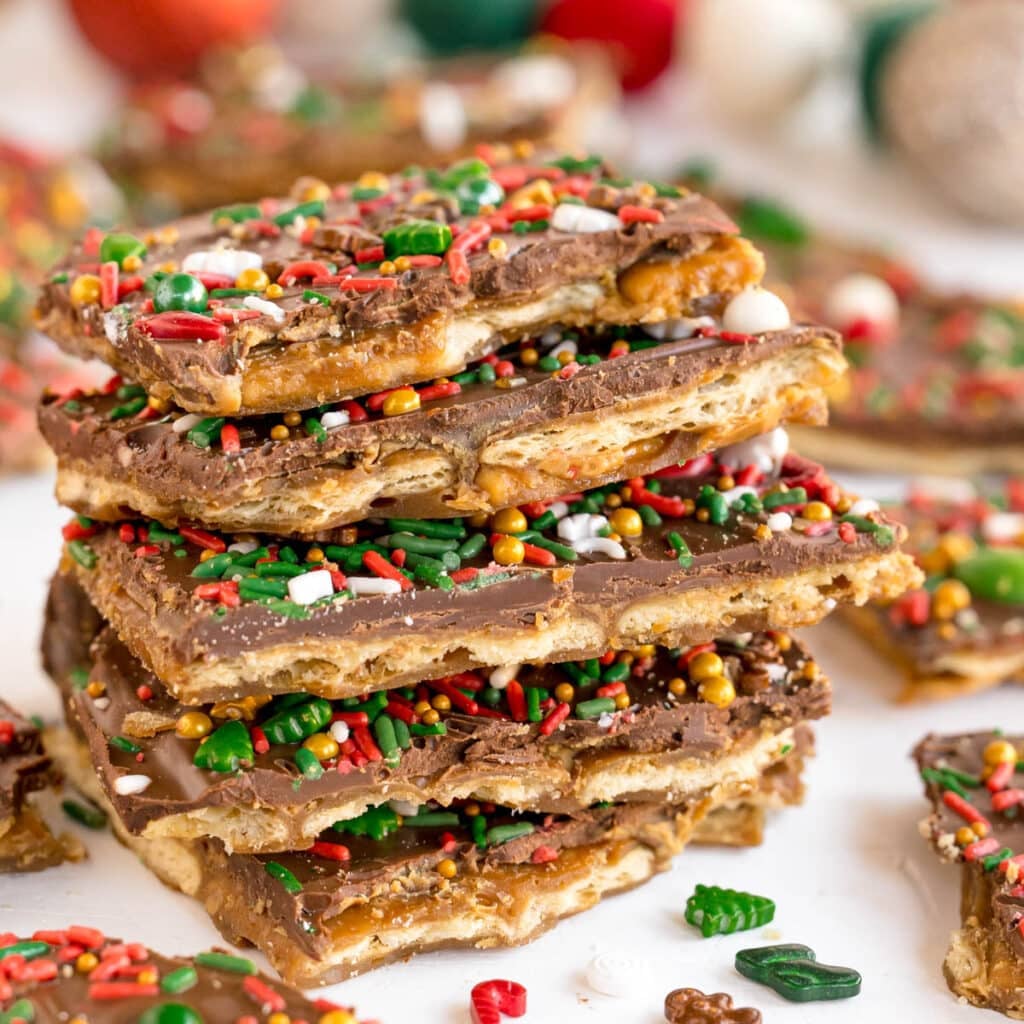 A close-up of a stack of layered Christmas crack, featuring saltine crackers topped with chocolate and decorated with festive red, green, and gold holiday sprinkles.