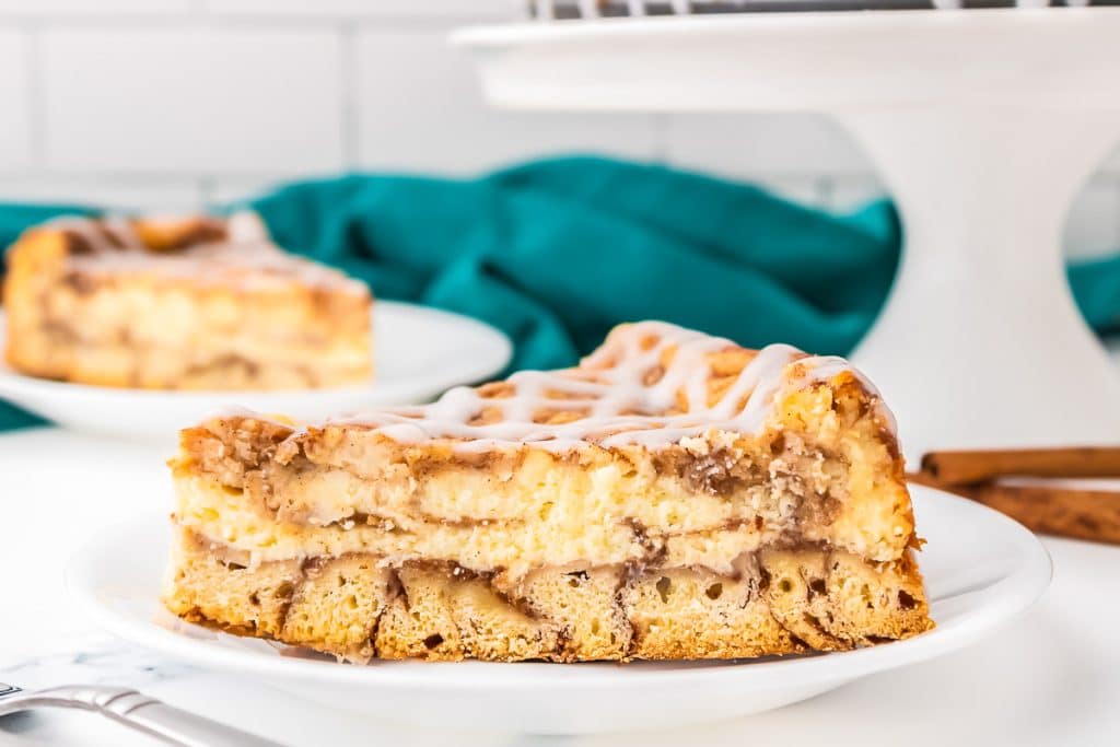 side view of a slice of cinnamon roll cheesecake on a white plate.