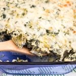 wooden spoon scooping spinach artichoke chicken casserole from a blue glass dish.