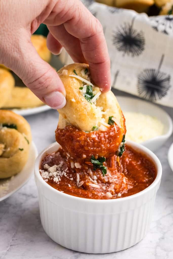 garlic knot dipping into marinara sauce.