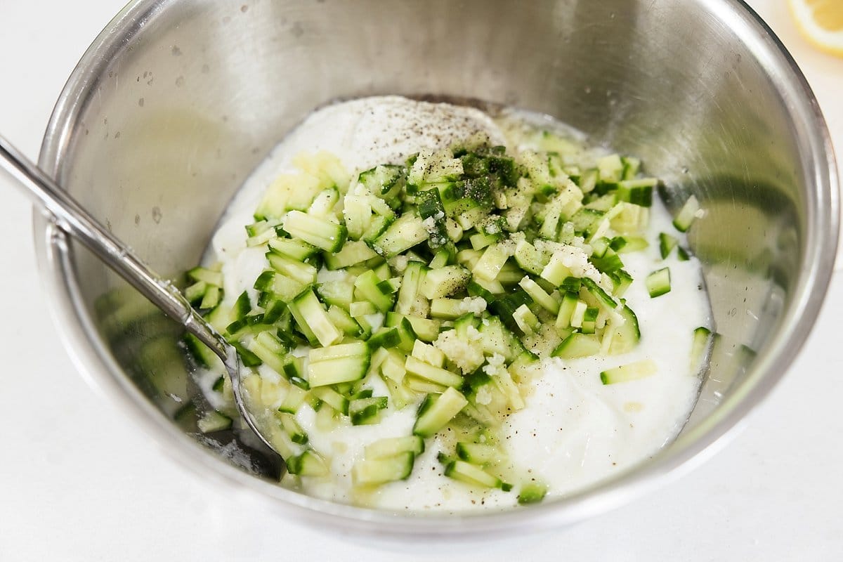 Ingredients for tzatziki sauce in a large metal bowl.