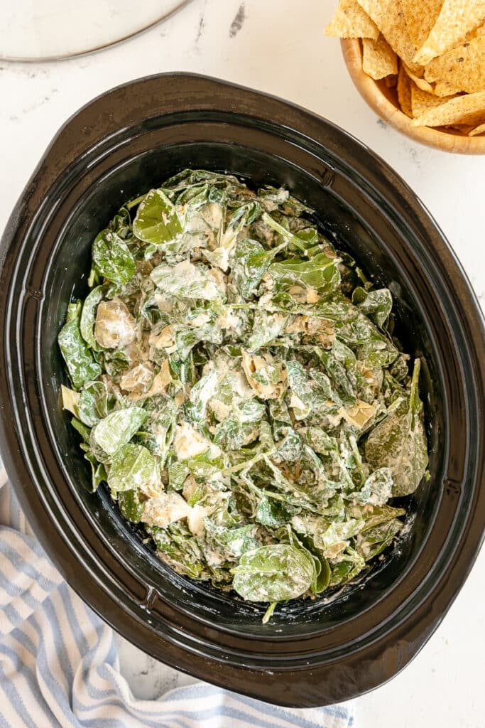 overhead shot of fresh spinach and ingredients in a slow cooker.