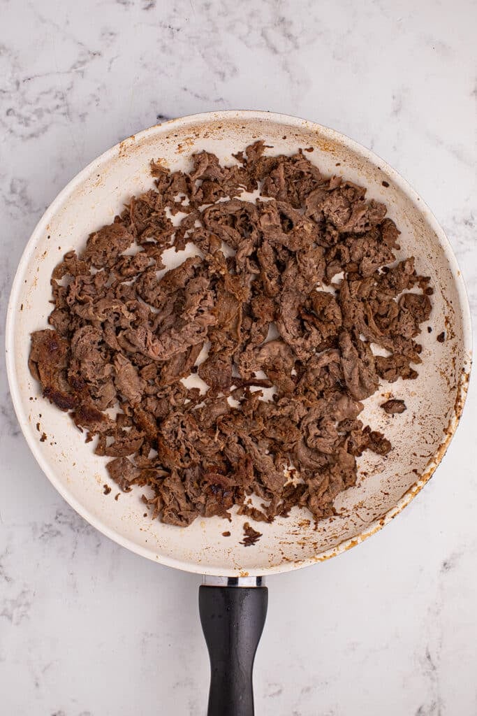 overhead shot of thinly sliced steak in a skillet.