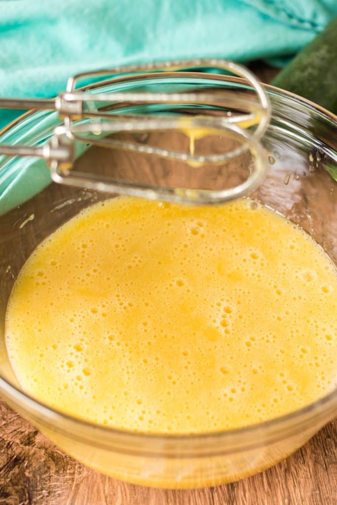 mixing bowl of yellow mixture under hand mixer beaters.