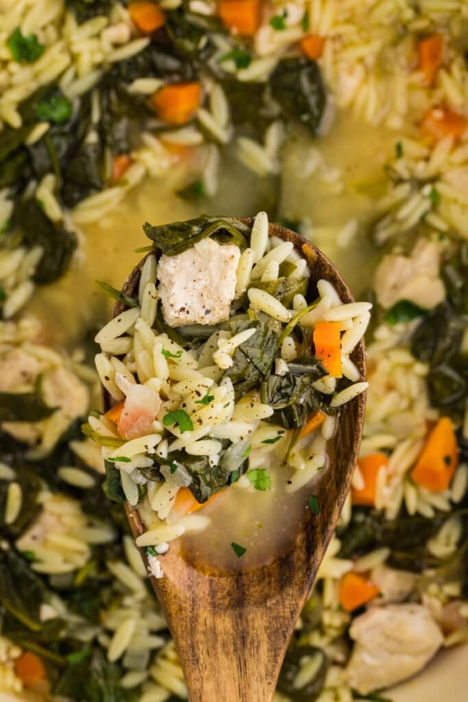 wooden spoon lifting a scoop of lemon chicken orzo soup.