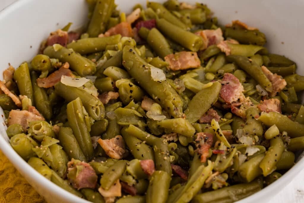 Close-up of green beans with bacon and onion in a white bowl.