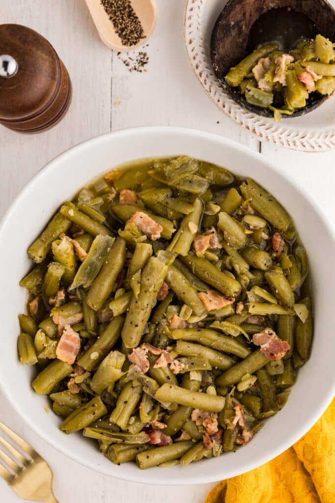 Bowl of green beans cooked with bacon and onion on a white table.
