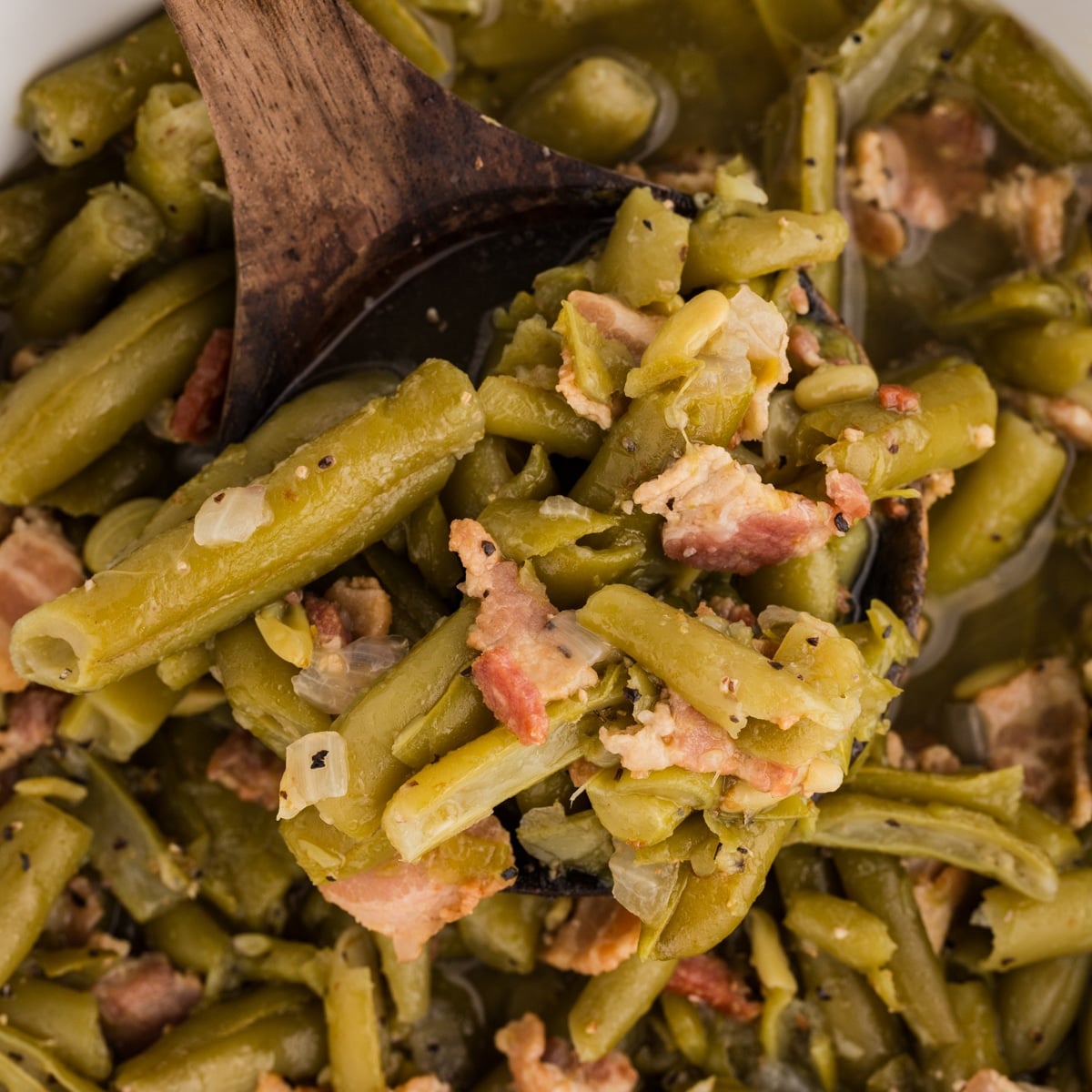 Green beans with bacon and onion on a wooden spoon over a pot.