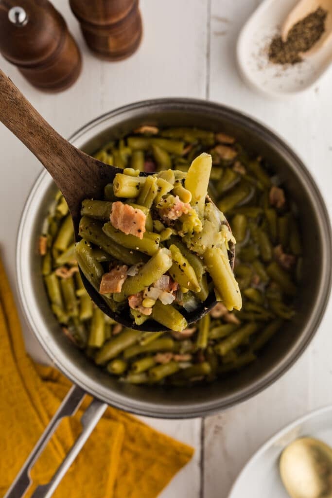 Green beans with bacon and onion on a wooden spoon over a pot.