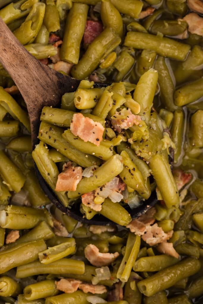 Green beans with bacon and onion on a wooden spoon over a pot.